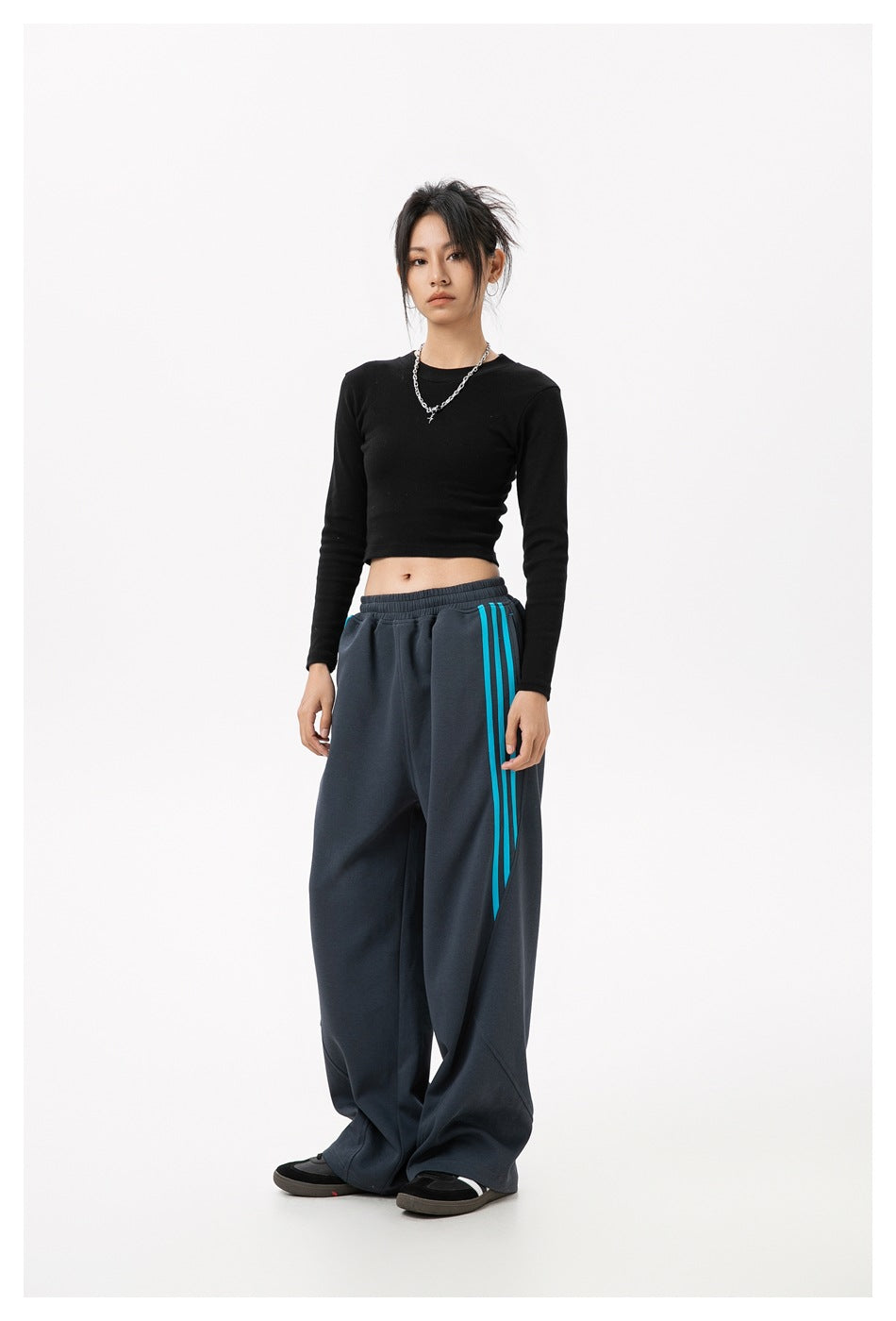 Full-length model wearing charcoal wide-leg track pants with an elastic waist and turquoise side stripes.