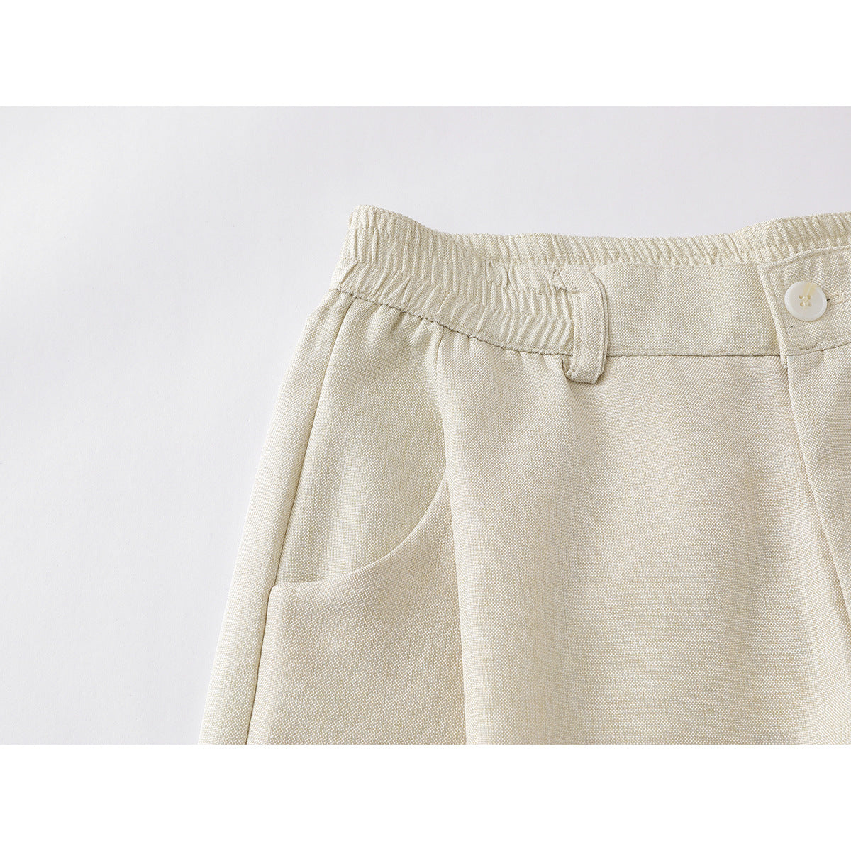 Close-up of cream wide-leg trousers showing an elasticized waistband, button, belt loop and curved pocket.