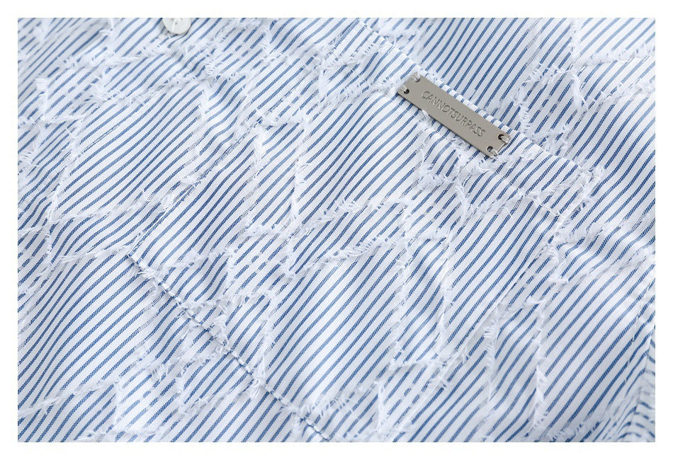 Close-up of white fabric with narrow blue stripes, frayed cutout details, and a small metal tag.