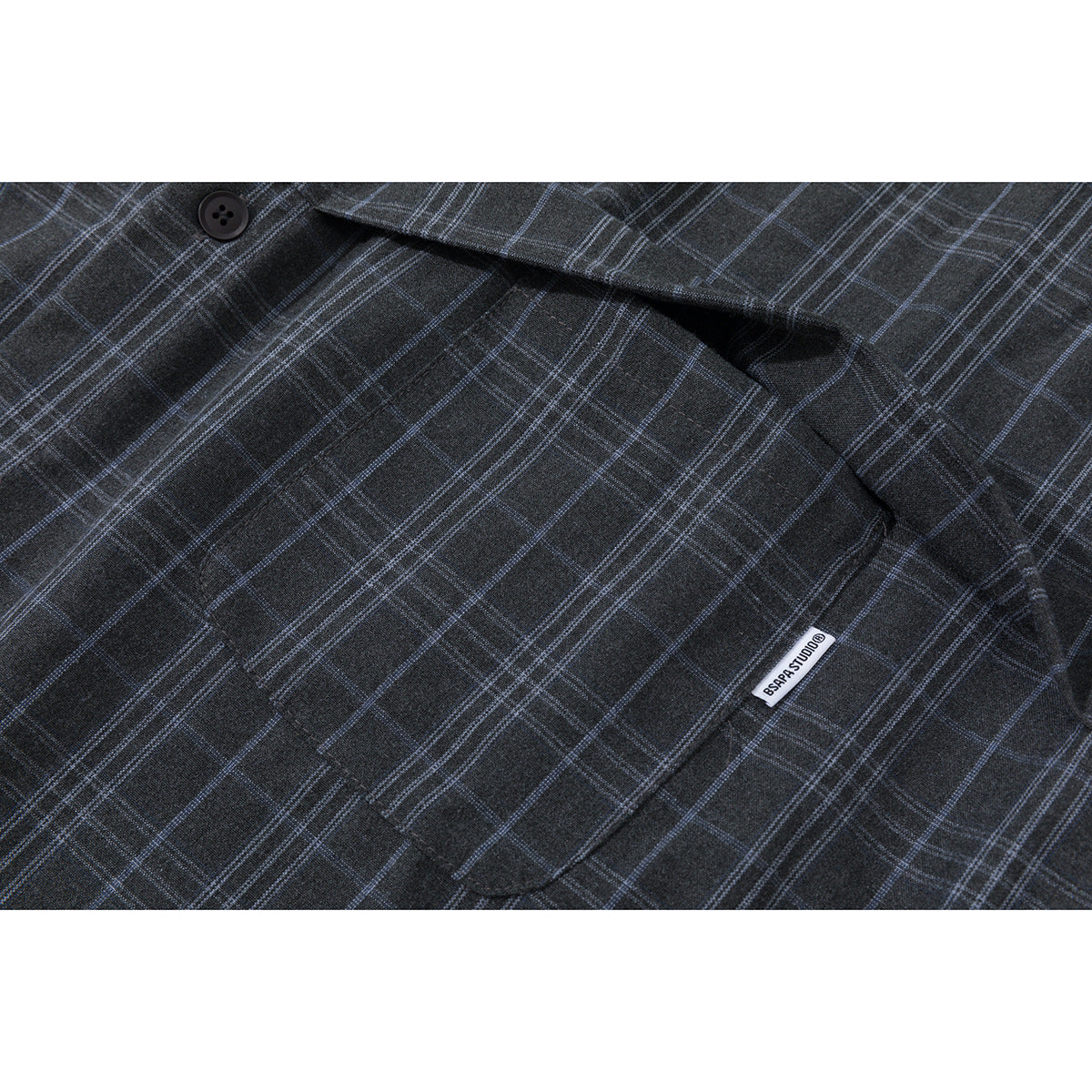 Close-up of a charcoal plaid shirt's chest pocket with a small woven label.