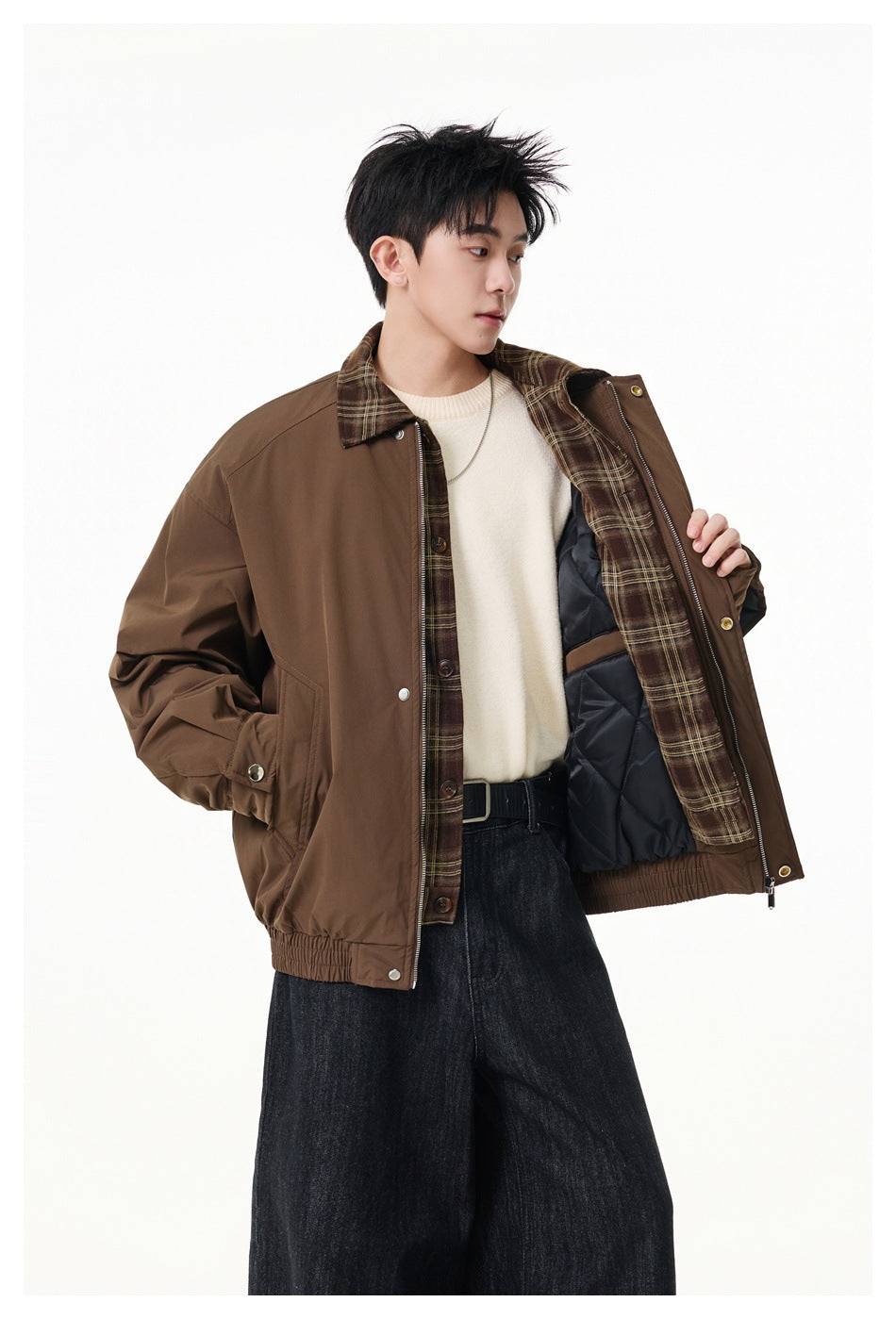 Model wearing an open brown jacket showing plaid inner layer and quilted black lining over a cream sweater