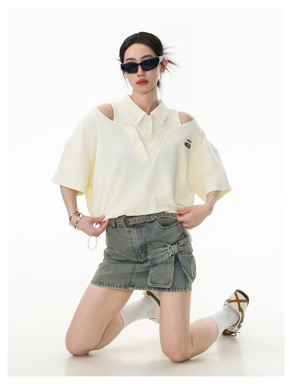 Model wearing an ivory cutout-shoulder polo and a gray denim mini skirt, kneeling.