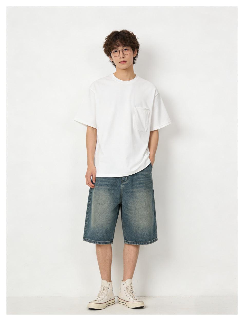 Full-length front view of a model in a white pocket T-shirt and loose blue denim shorts.