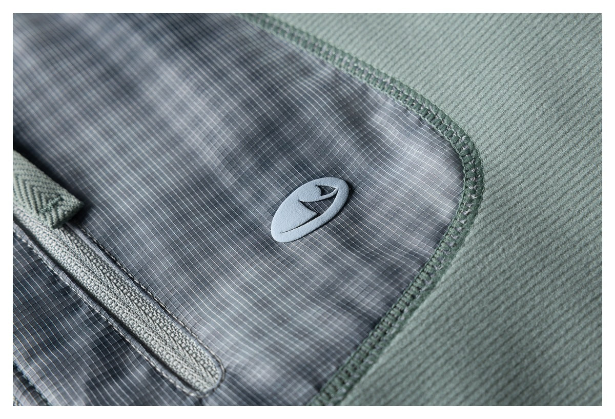 Close-up of a gray grid-patterned pocket panel, stitched onto sage-green fabric, with a small emblem.