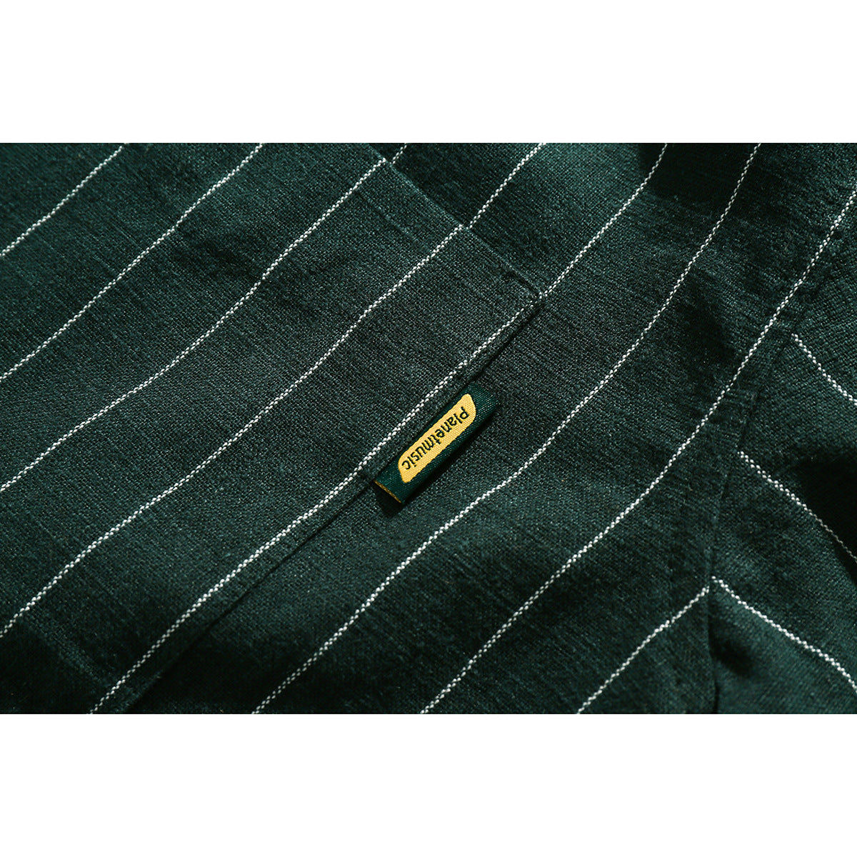 Close-up of a small yellow woven label on dark green fabric with thin white pinstripes.