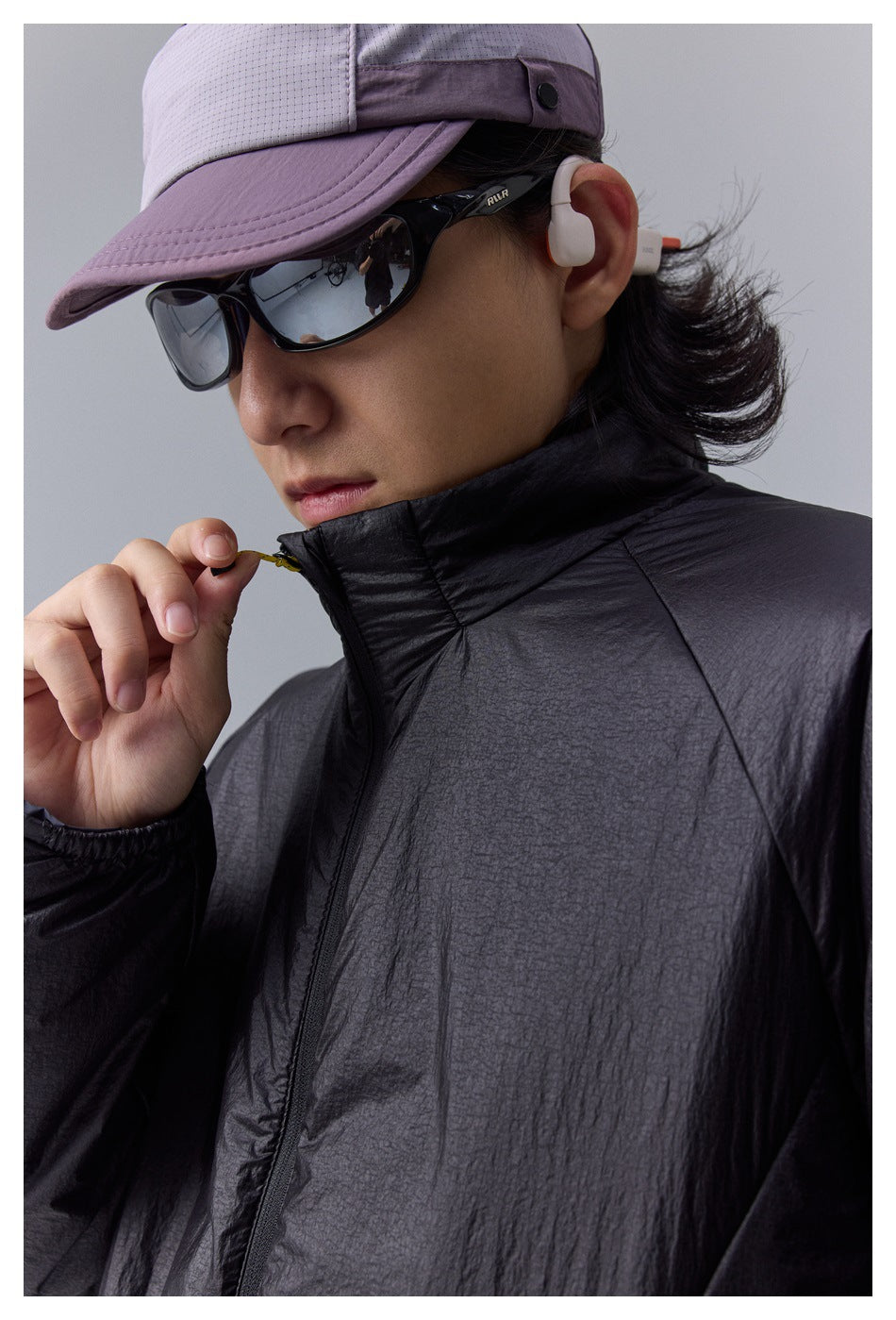 Close-up of a black jacket’s high collar and zipper as the model adjusts it.