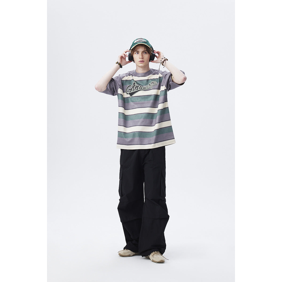 Full-length model wearing a gray, teal, and cream striped oversized T-shirt with chest lettering and black cargo trousers.