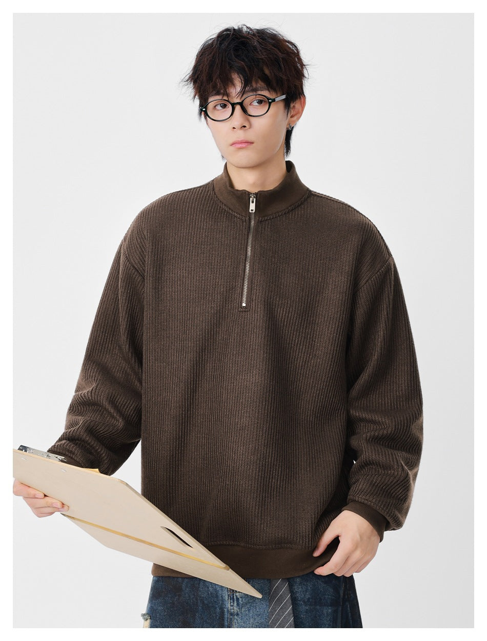 Front view of a model wearing a brown textured half-zip pullover with a stand collar and ribbed hem.