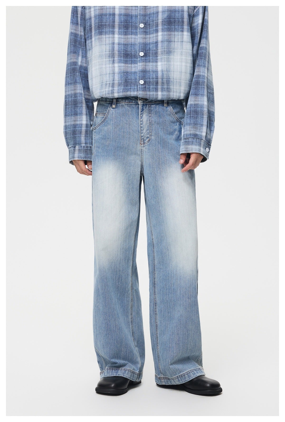 Person wearing light blue washed wide-leg jeans with a blue plaid shirt and black boots, front view