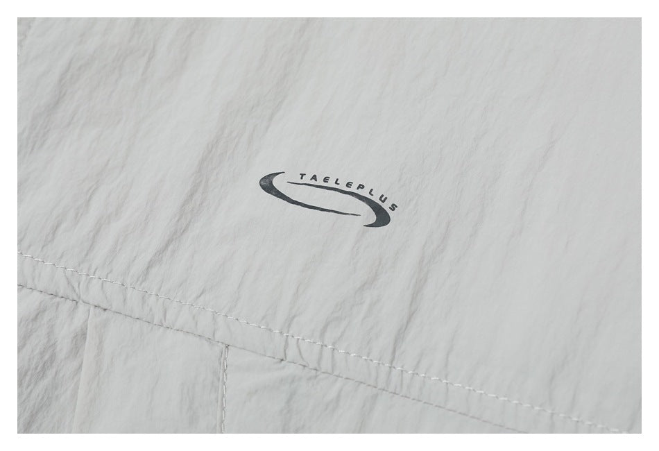 Close-up of a small dark TAELEPLUS logo printed on light gray jacket fabric.