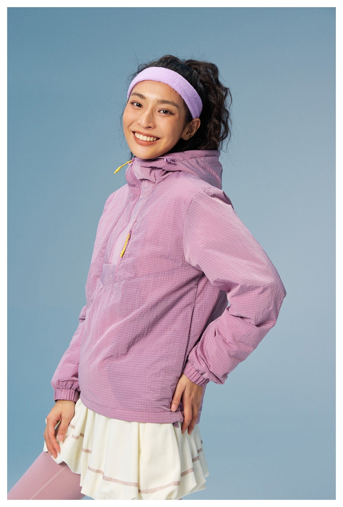 Model wearing a lilac grid-pattern hooded pullover with yellow zipper pulls, a white skirt, and lilac leggings.