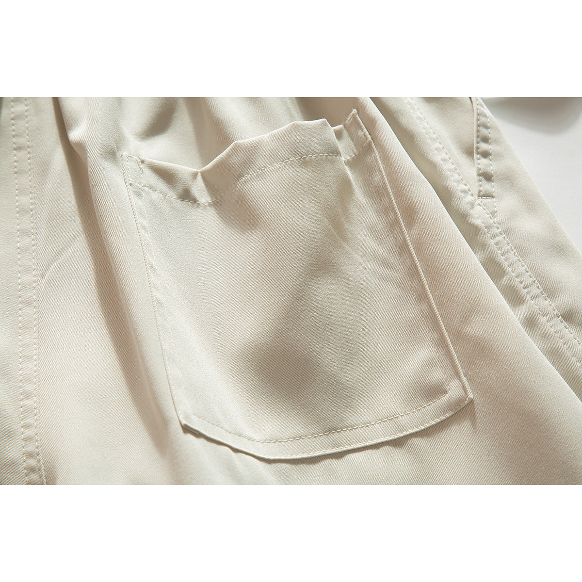 Close-up of cream shorts showing a large rectangular patch pocket and surrounding seam details.