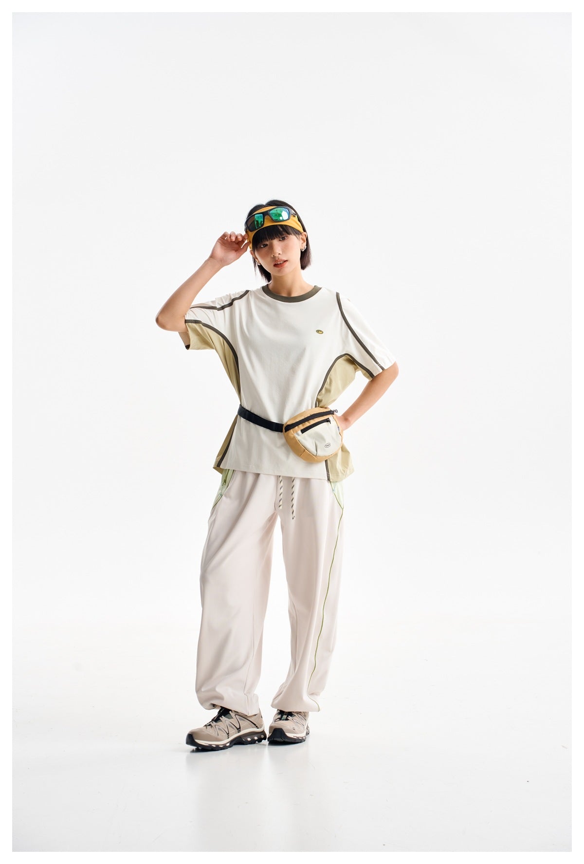 Model wearing a white short-sleeve shirt with olive and dark trim, loose light pants, and a waist pouch.