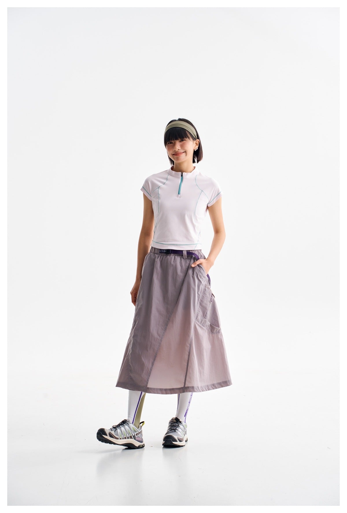 Model wearing a white zip-neck top with teal seam accents and a gray-lilac wrap skirt.