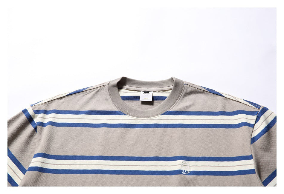 Close-up of the striped T-shirt’s crew neck, shoulder, chest, and small white embroidered emblem.