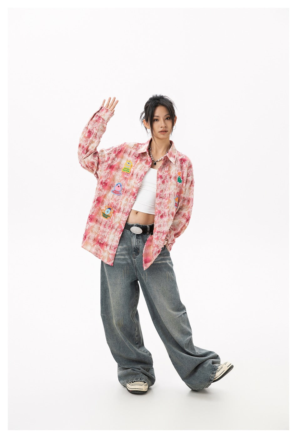 Model wearing open pink tie-dye plaid shirt with monster patches over a white top and wide-leg jeans