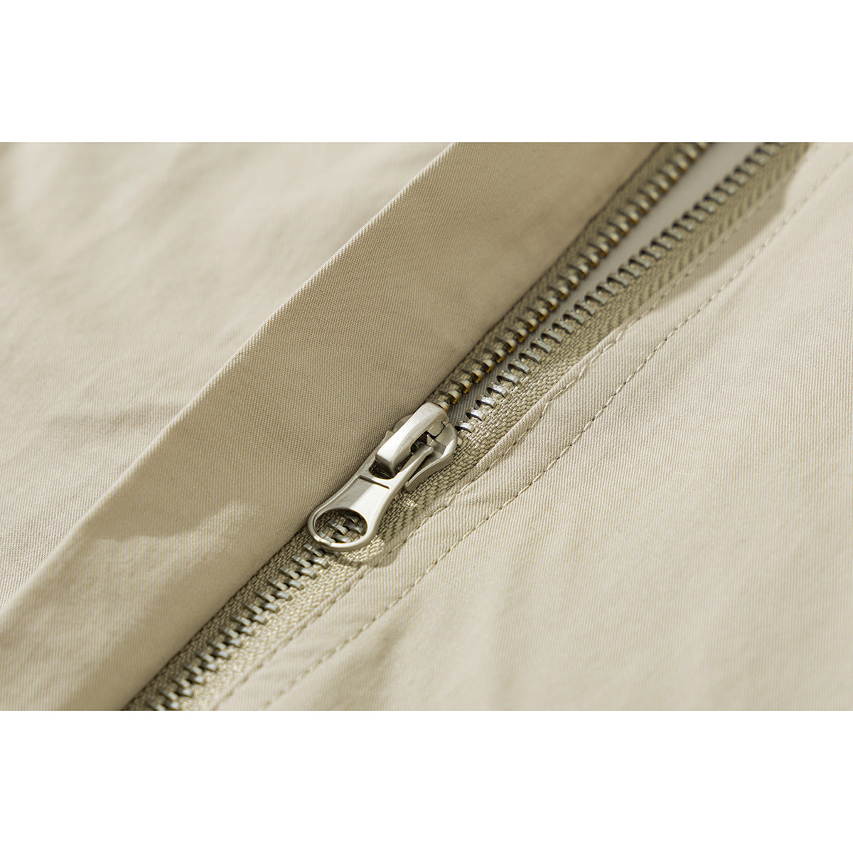 Close-up of a beige jacket's metal zipper and stitched placket.