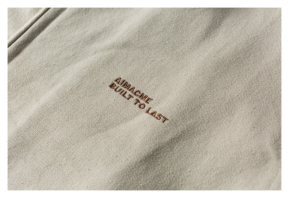 Close-up of brown embroidered text reading “AVAILABLE BUILT TO LAST” on beige fabric.