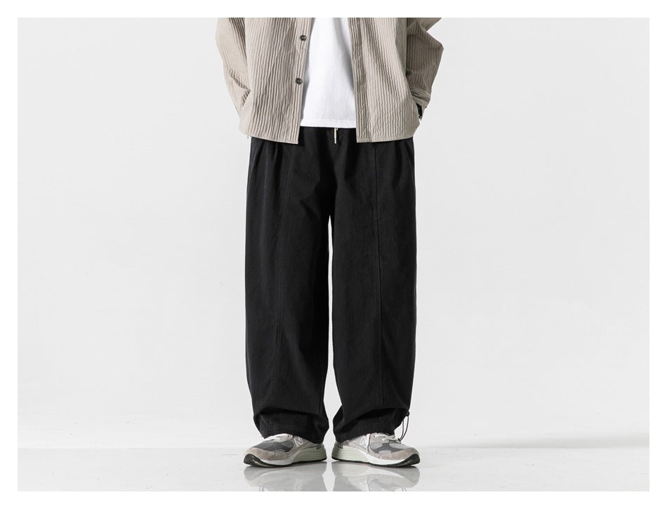 Model wearing black wide-leg pants with a beige ribbed shirt, white tee and gray sneakers, front view