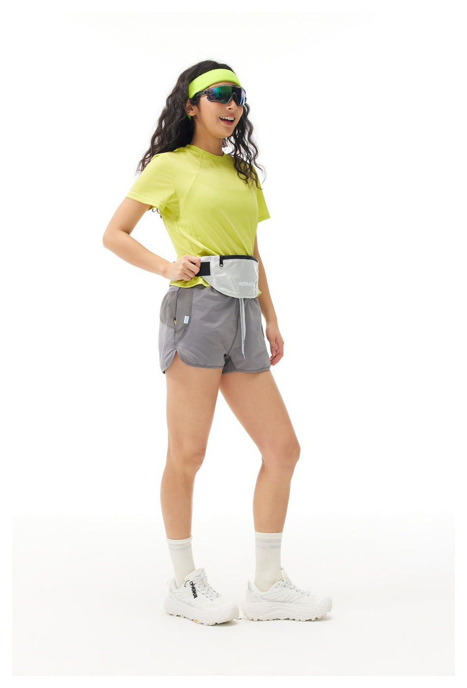 Three-quarter view of a model in a lime shirt, gray shorts, and a light waist pack.
