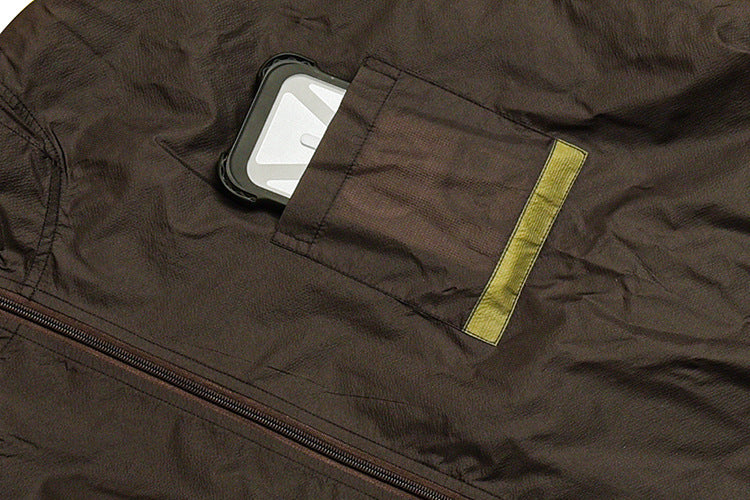 Close-up of a dark garment pocket holding a phone, with a yellow-green vertical tab.