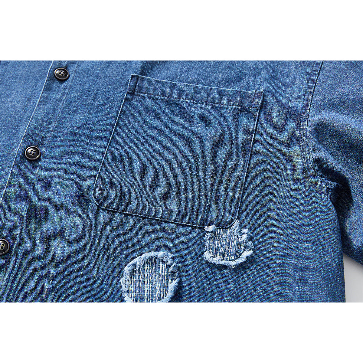 Close-up of a blue denim shirt’s chest pocket, dark buttons and two frayed circular patches.