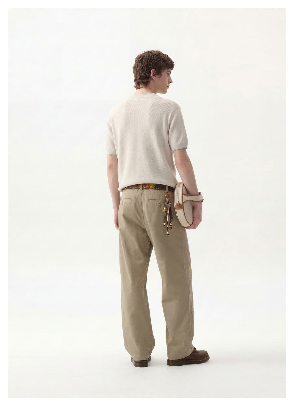 Back view of a model wearing an off-white short-sleeve top and khaki trousers, carrying a cream shoulder bag.
