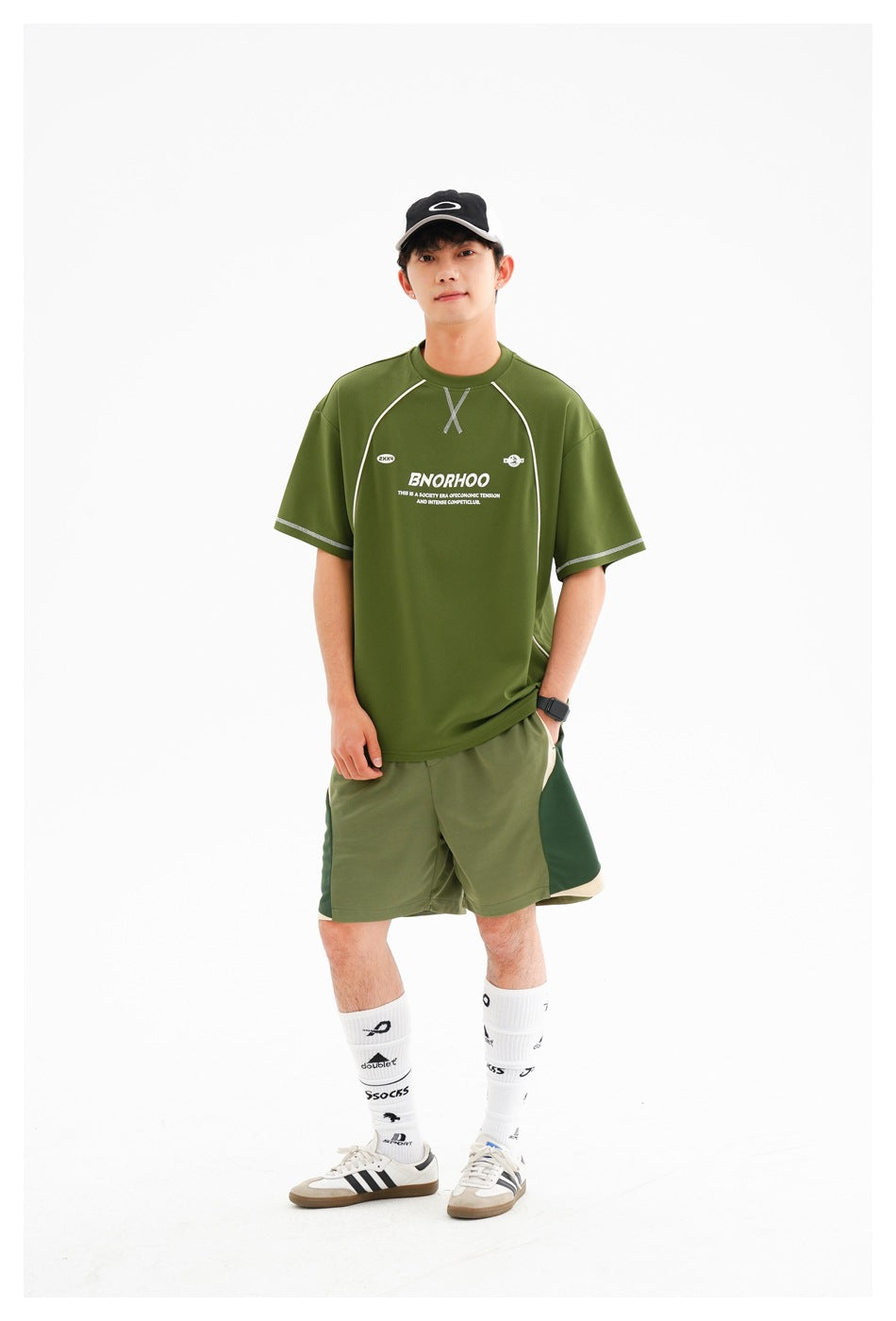 Person wearing a green short-sleeve T-shirt with white piping and chest print, green shorts, cap, white socks and sneakers