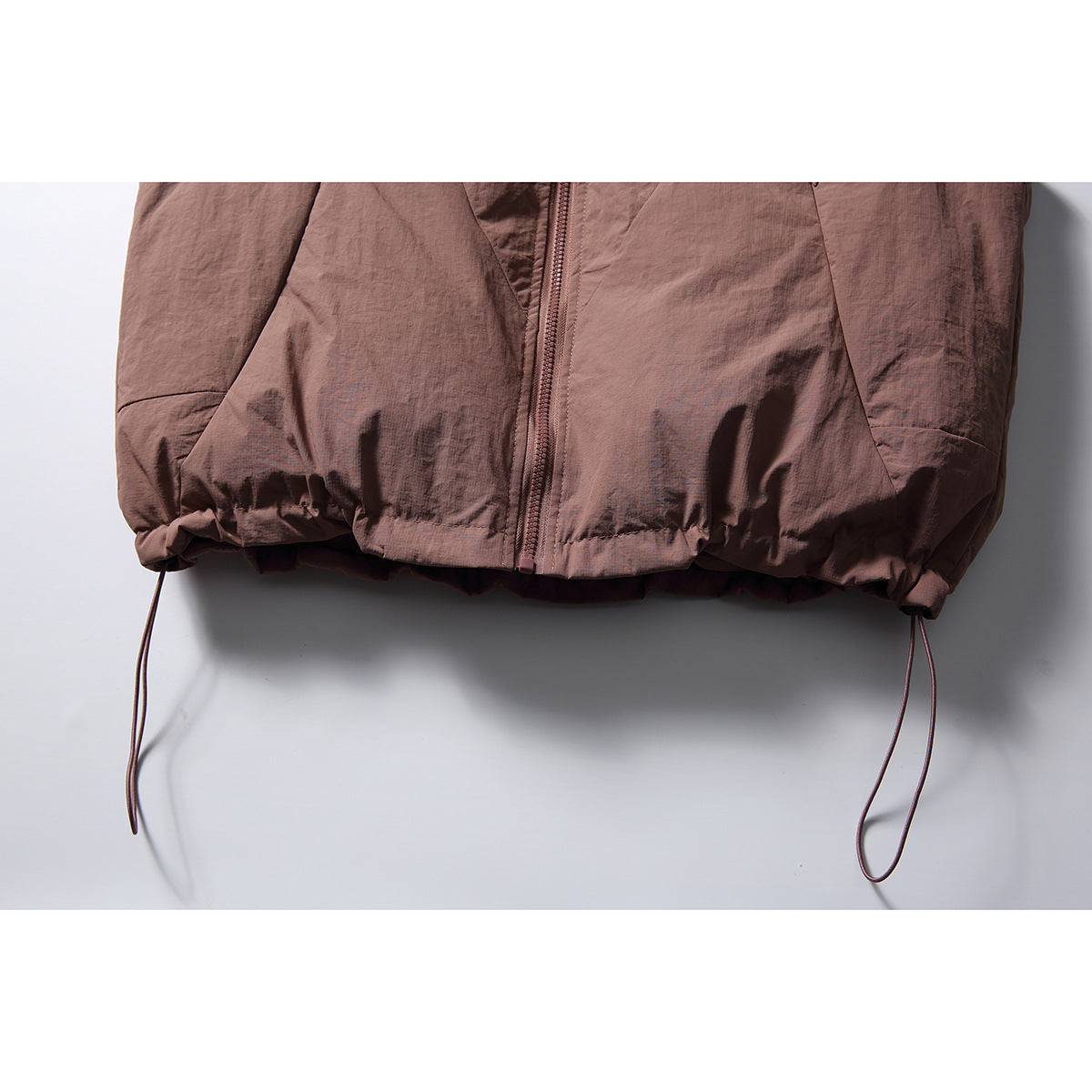 Close-up of the mauve vest’s gathered hem, central zipper, and adjustable hanging drawcords.