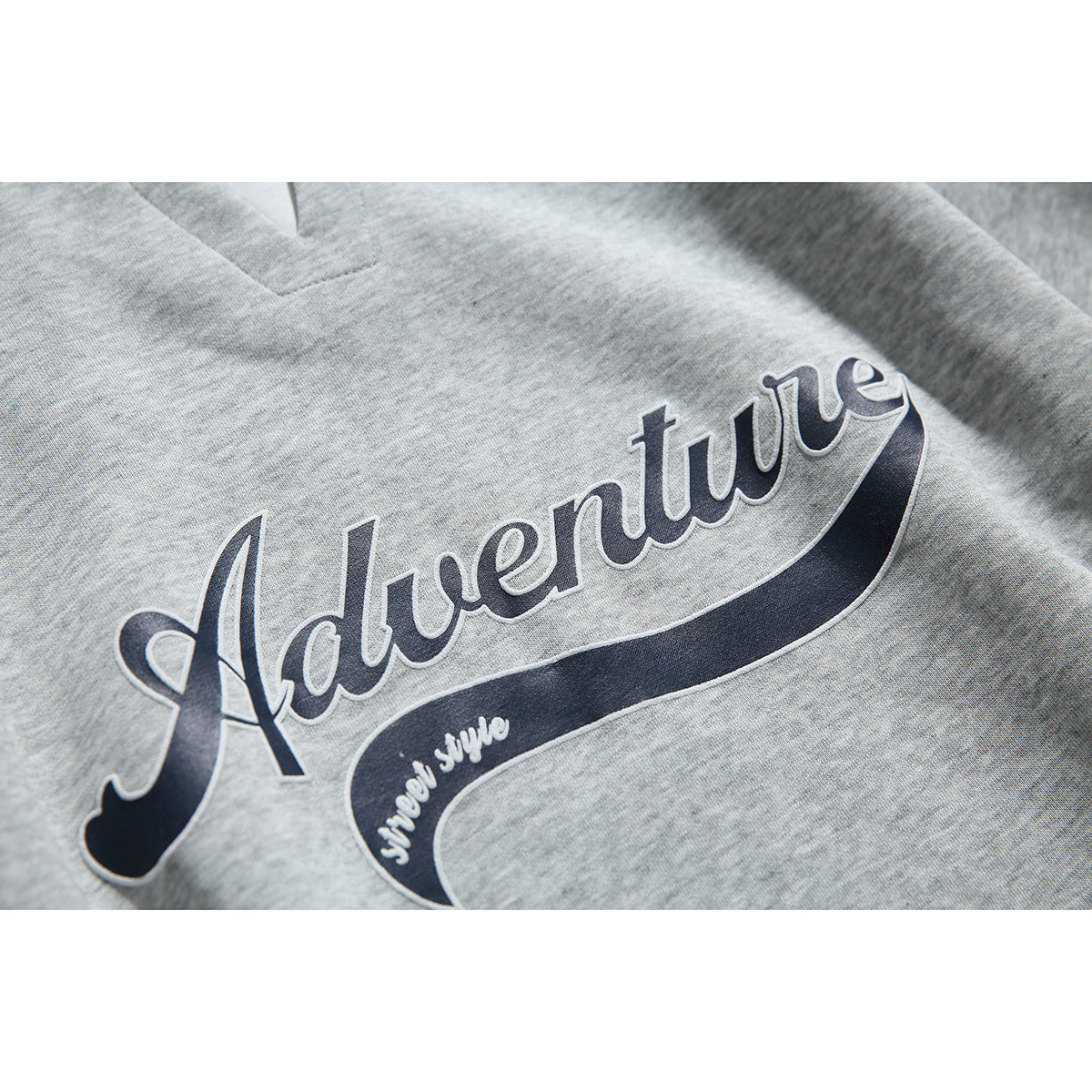Close-up of the navy “Adventure” script graphic printed on heather-gray sweatshirt fabric.