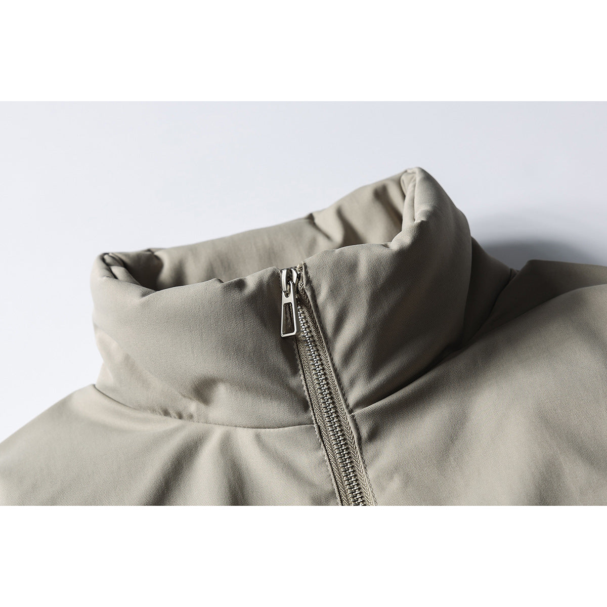 Close-up of a gray-beige jacket's tall stand collar and metal front zipper.
