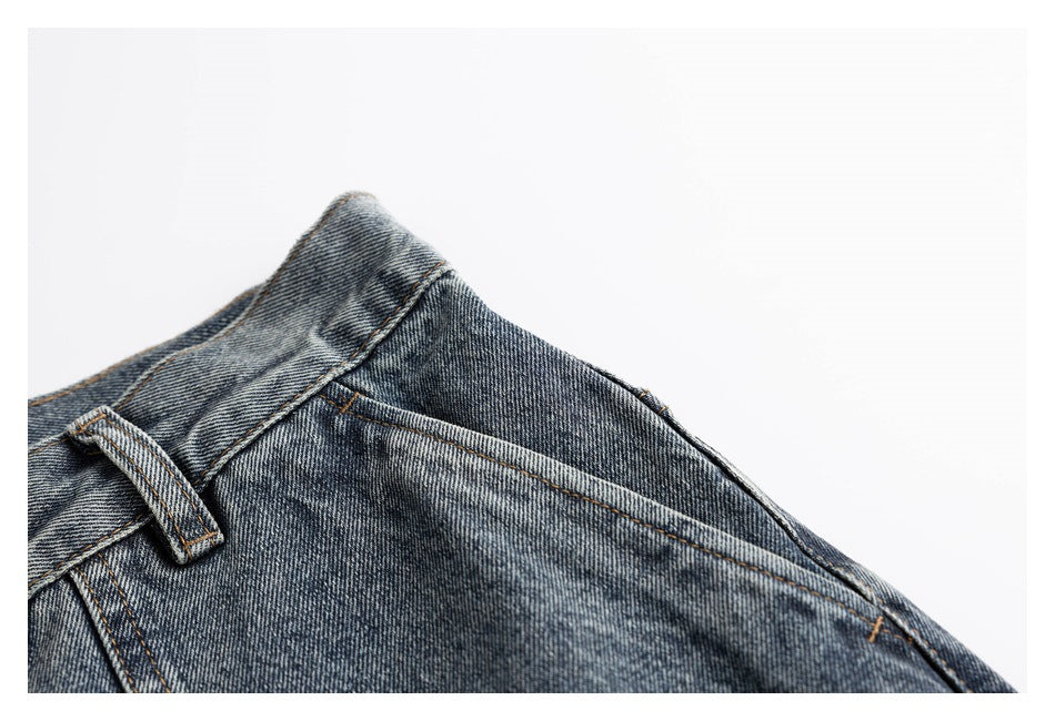 Close-up of washed blue-gray jeans showing a slanted front pocket, waistband, and belt loop.