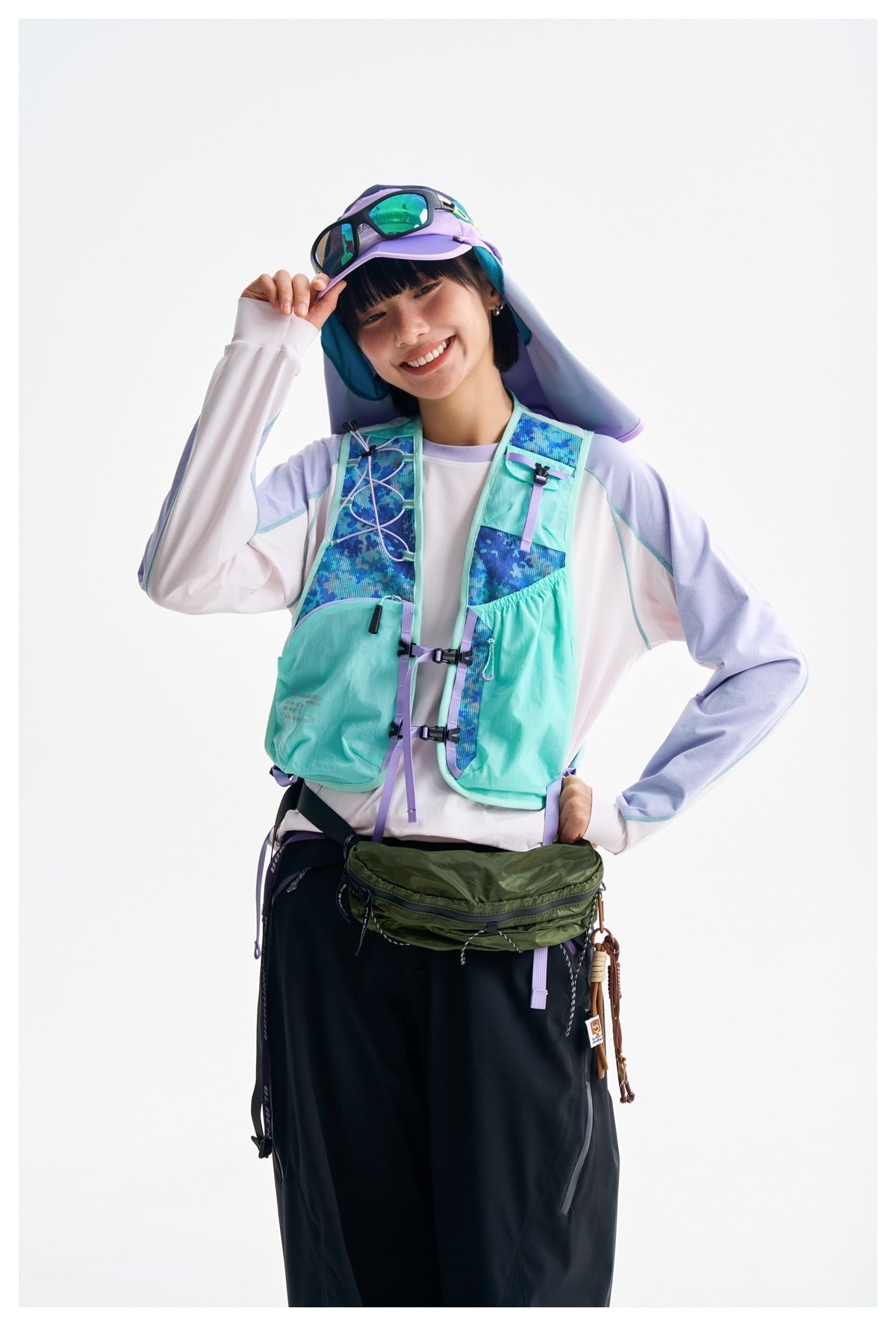 Model wearing a mint hiking vest with blue patterned panels and lavender straps, shown with a cap and sunglasses.
