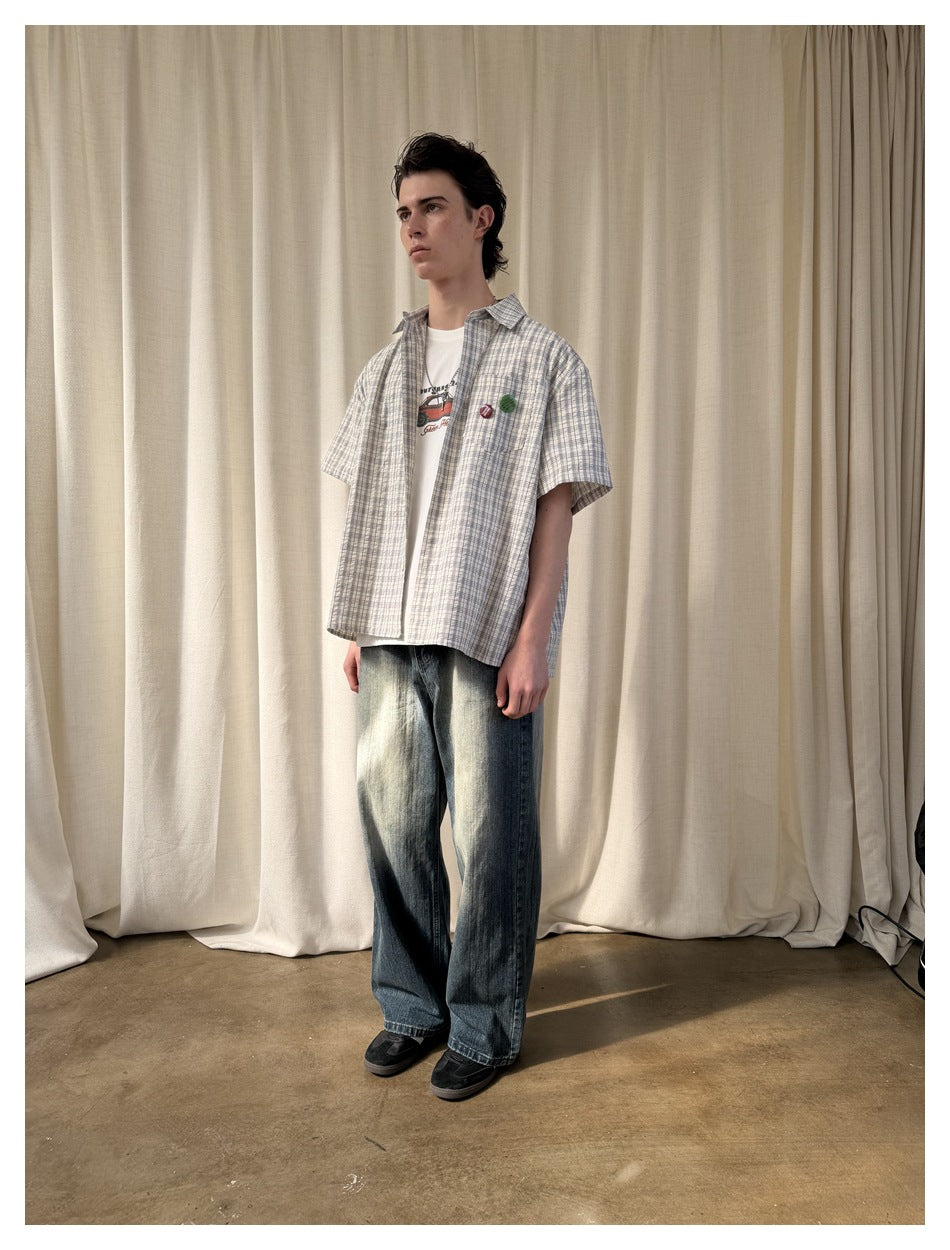 Model wearing open plaid short-sleeve shirt over a white graphic tee with wide-leg jeans, front view