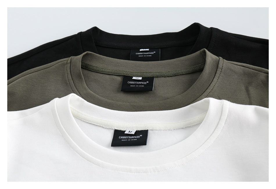 Close-up of the collars and neck labels on black, olive-green, and white crewneck tops.