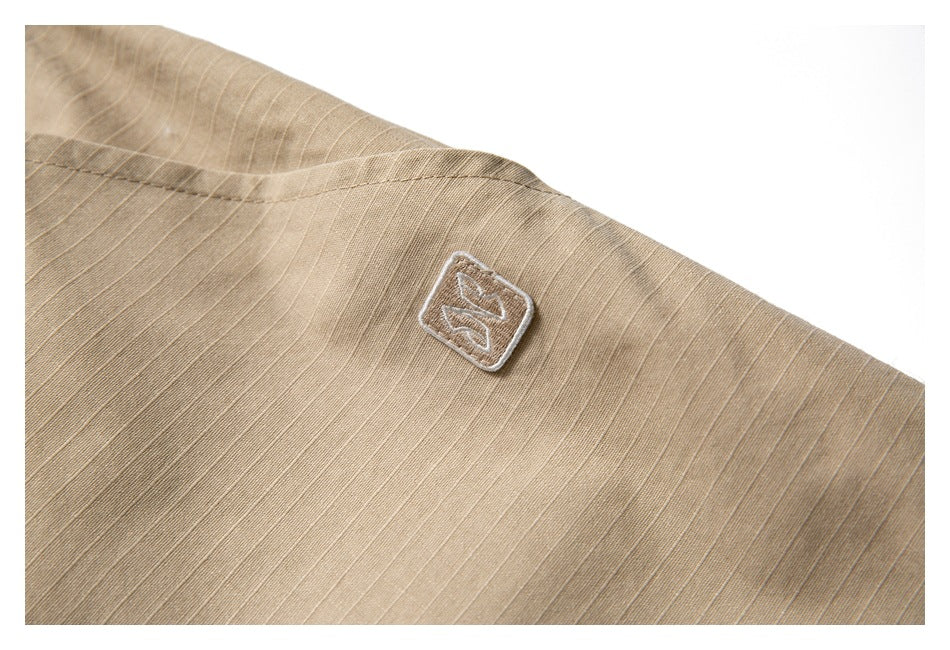 Close-up of tan ripstop fabric showing a small embroidered square patch and seam.