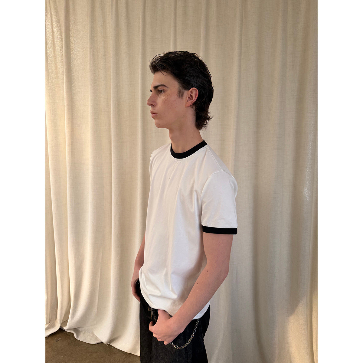 Side view of a model wearing a white T-shirt with black ribbed collar and sleeve bands.