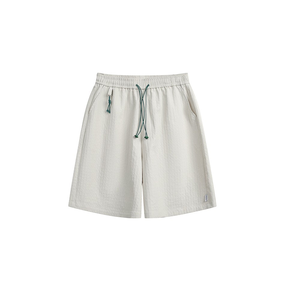 Off-white textured knee-length shorts with elastic waistband, green drawstring cord and side pockets, flat front view