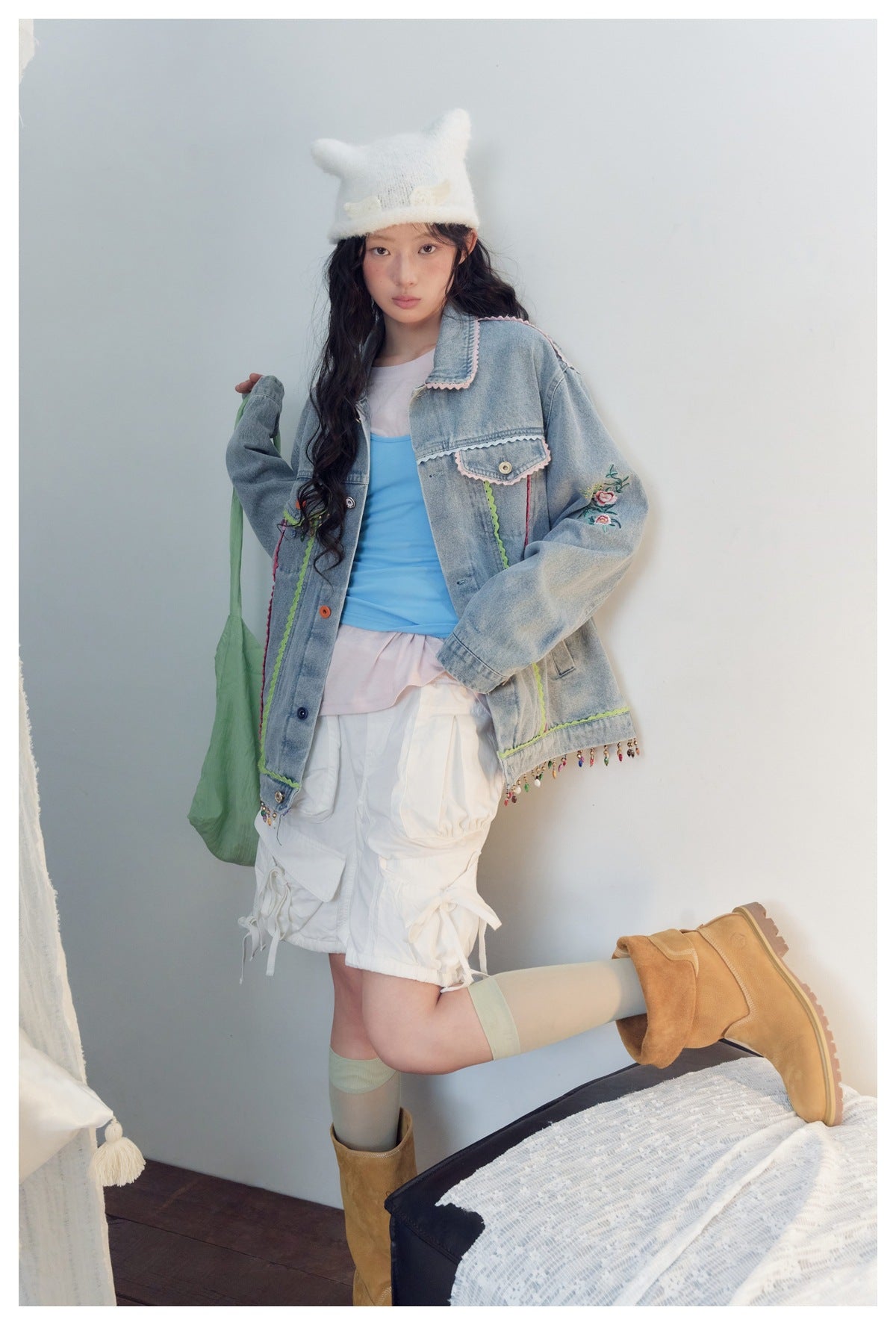 Model poses in a light-blue denim jacket with floral embroidery, colorful trim and dangling beads.