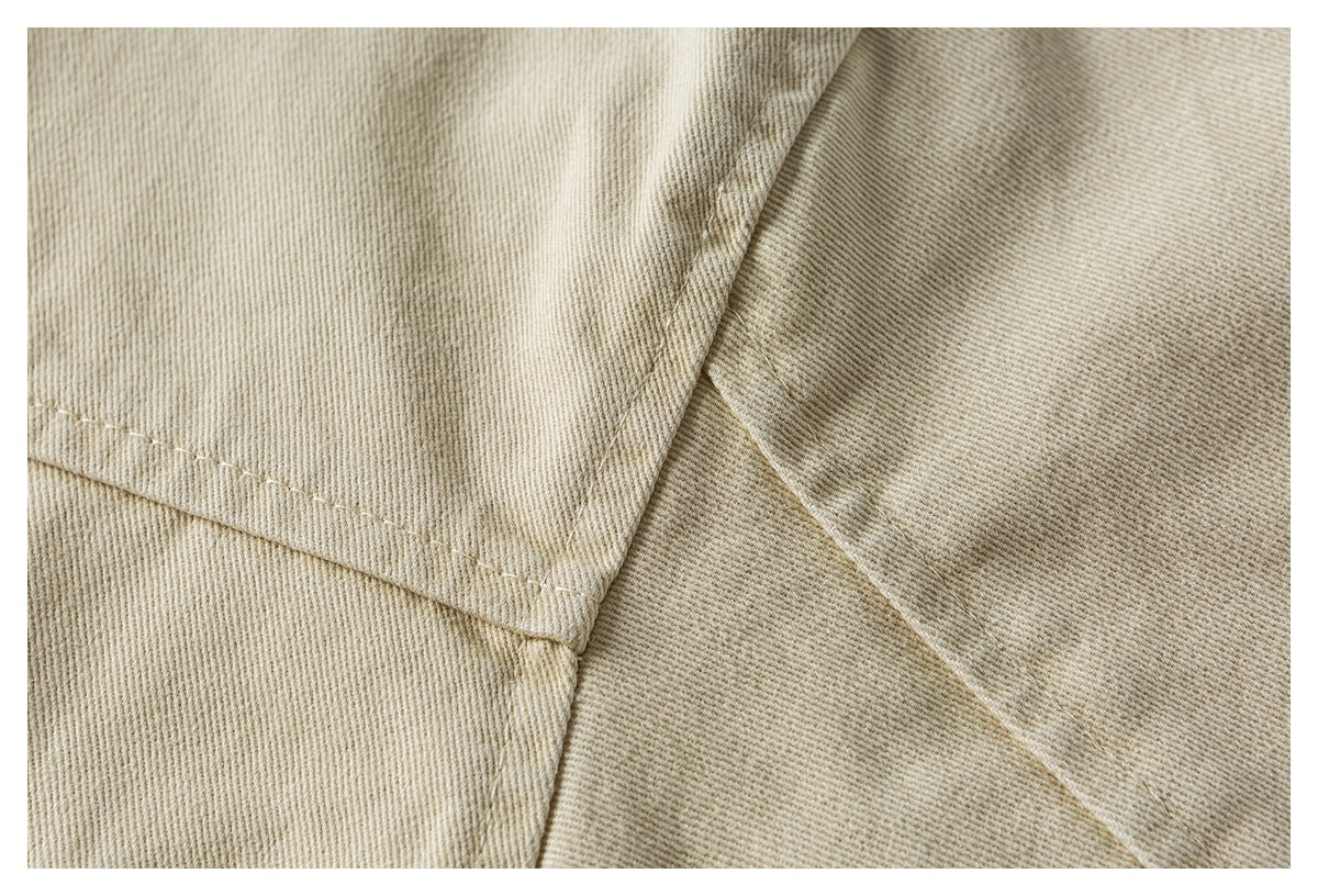 Close-up of beige twill jacket fabric with an overlapping panel and stitched seam.