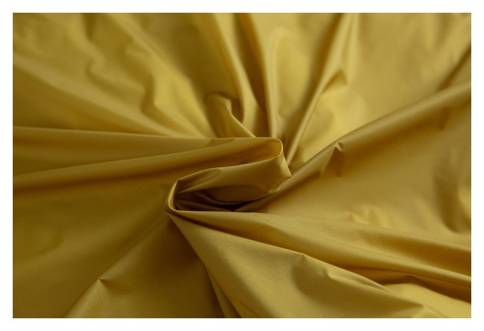 Close-up of mustard-yellow garment fabric gathered into folds, showing its fine texture.