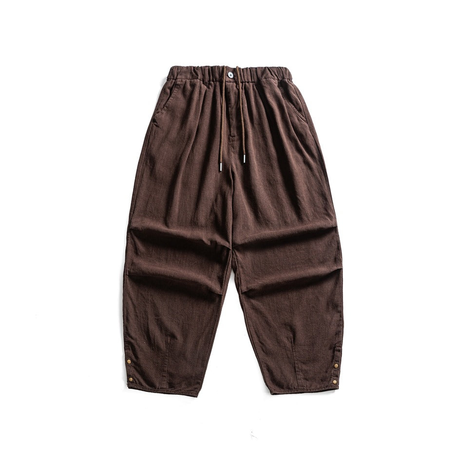 Brown wide-leg textured pants flat lay with drawstring elastic waist, button and metal snaps at the hems