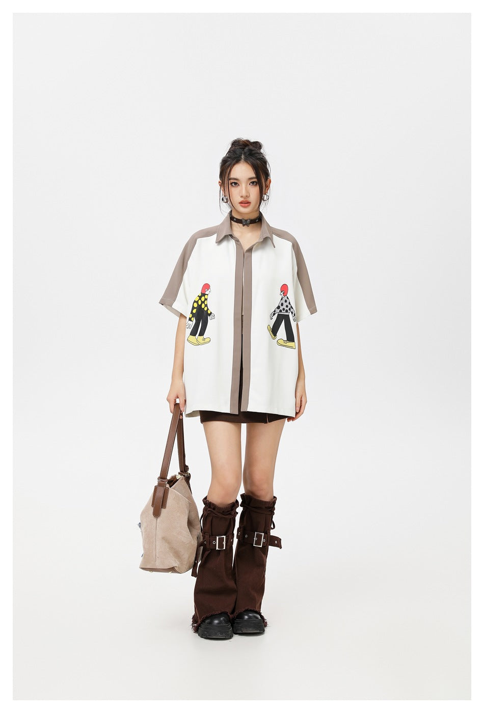 Full-length front view of a model wearing a white graphic shirt with taupe trim and carrying a beige bag.