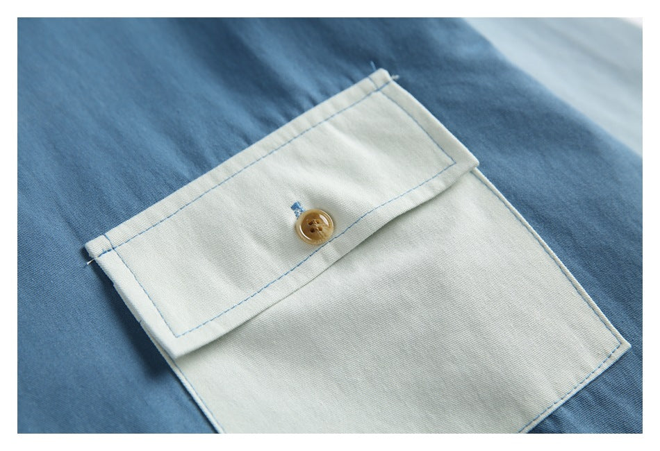 Close-up of a pale flap pocket with blue stitching and a tan button on blue shirt fabric.