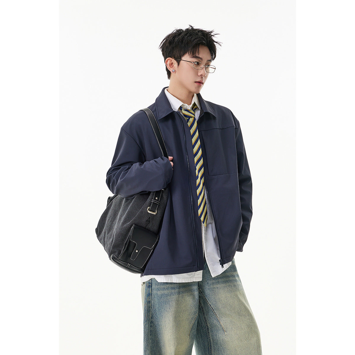 Model wearing a navy zip-front jacket over a white shirt and striped tie, with loose faded jeans.