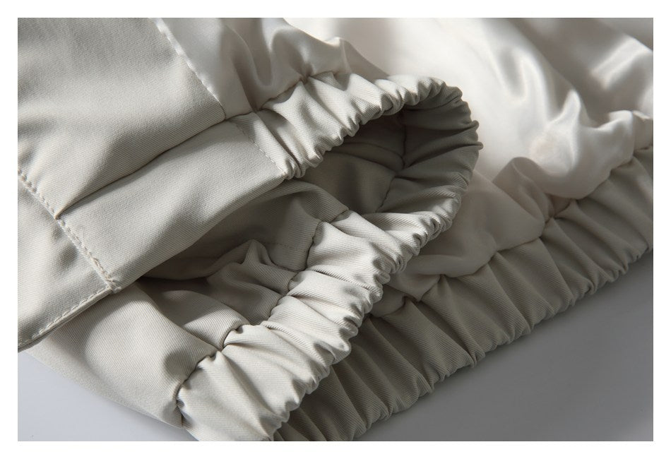 Close-up of a gathered elastic opening and stitched panels on an off-white garment.