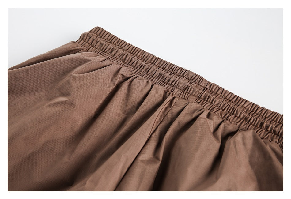 Close-up of the gathered elastic waistband and pleated fabric on brown shorts.