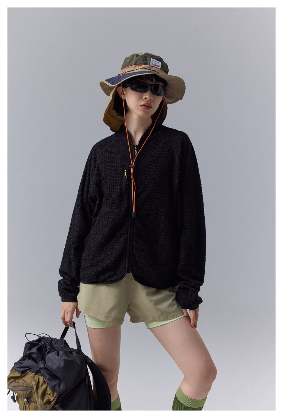 Front view of a model wearing a black textured zip jacket over khaki shorts.