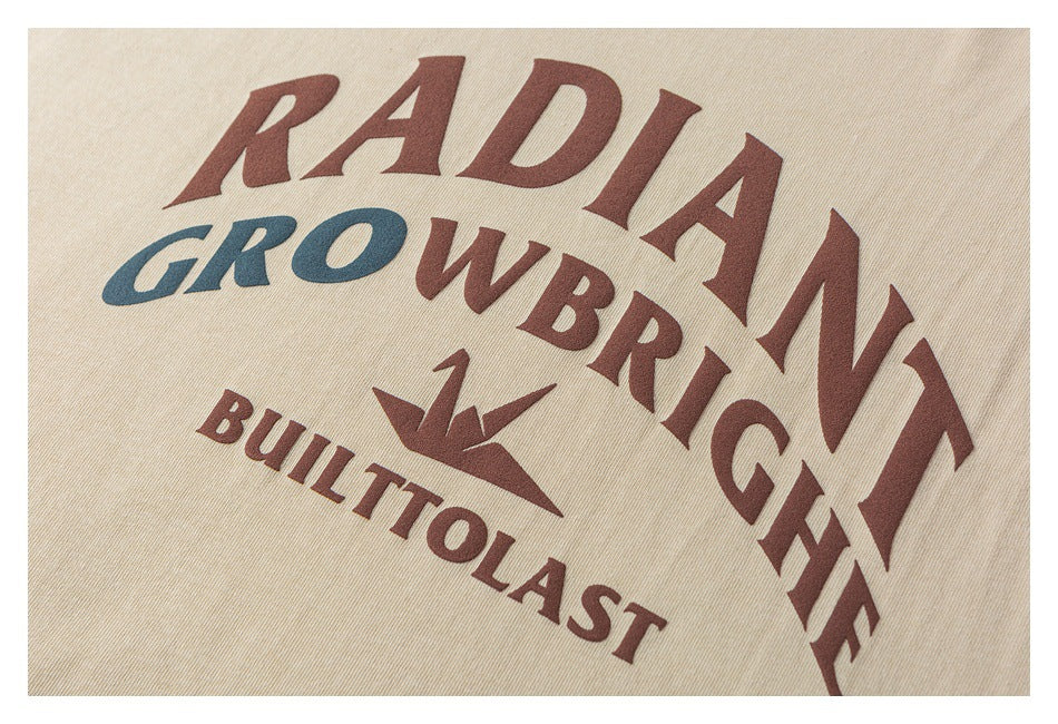 Close-up of the beige T-shirt's chest graphic with burgundy and blue lettering and a small origami-style bird.