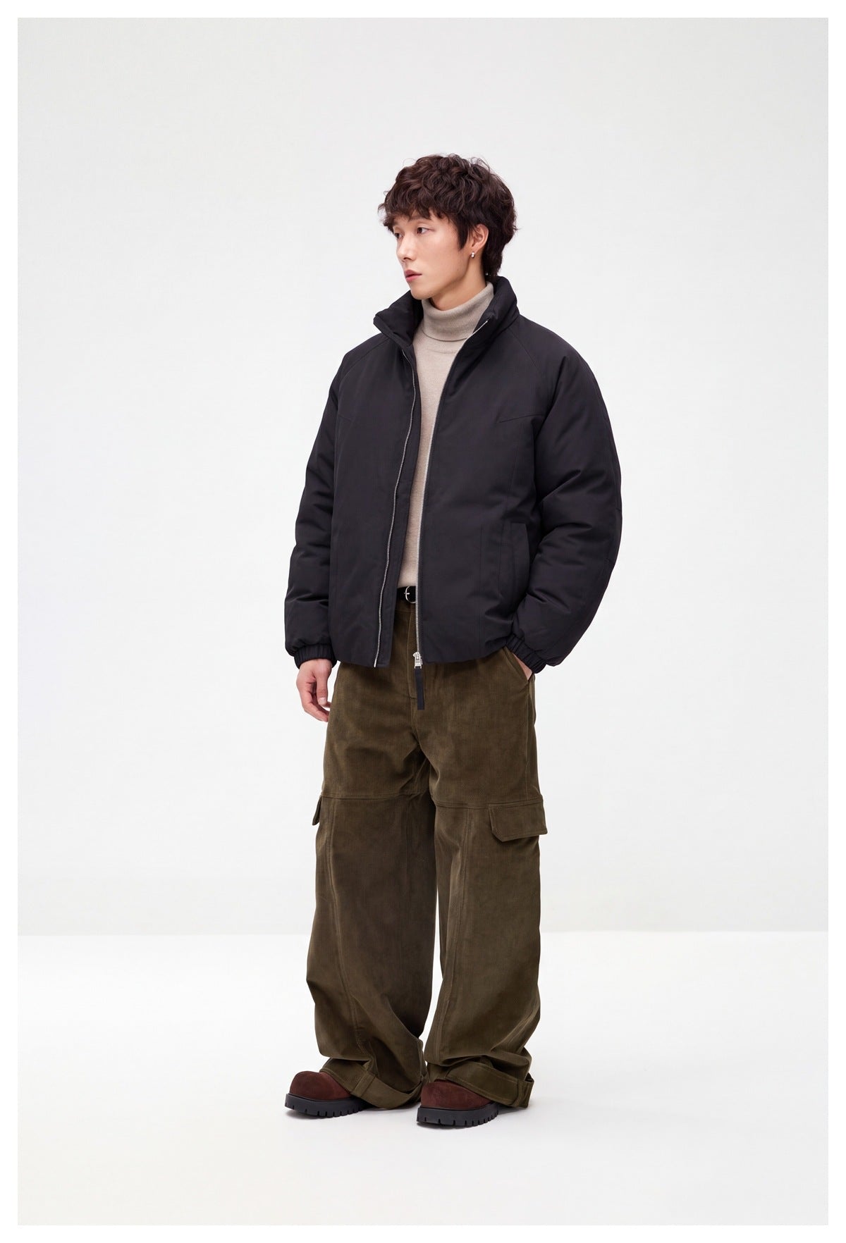 Model wearing a black zip-front jacket with a raised collar and olive cargo trousers, shown at a three-quarter angle.